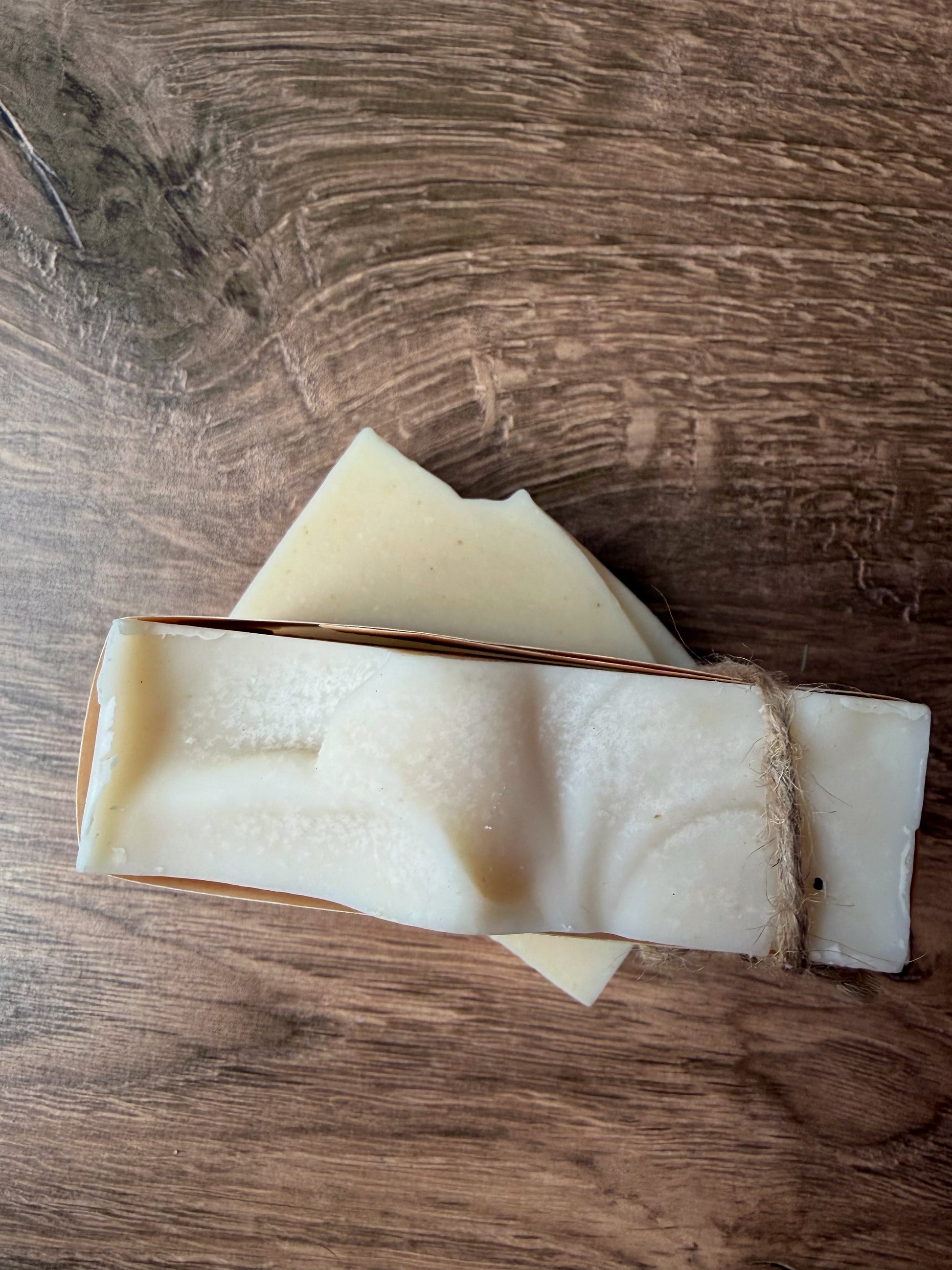 Two Lil Daisy Soaps Unscented Coconut Milk & Aloe bars, one with twine, sit on a wooden surface.