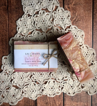 Lil Daisy Soaps Velvet Rose Goat Milk Soap bar displayed on a lace doily atop a wooden surface.
