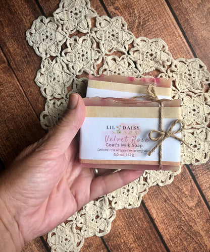 Hand holding Velvet Rose Goat Milk Soap by Lil Daisy Soaps, tied with twine on a crocheted doily.
