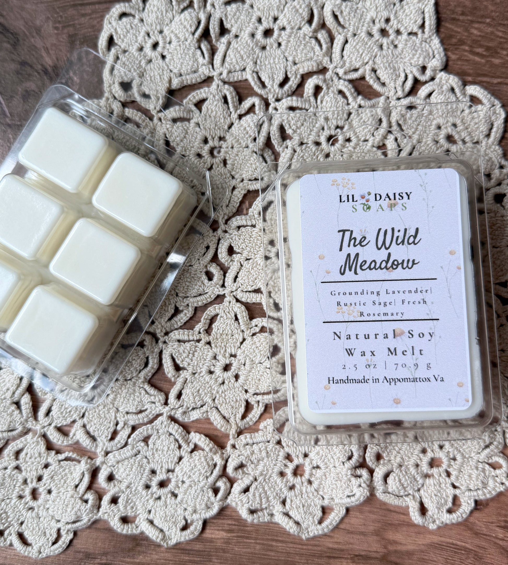 Two Lil Daisy Soaps wax melt packs rest on lace, one Wild Meadow with herbal lavender fragrance.