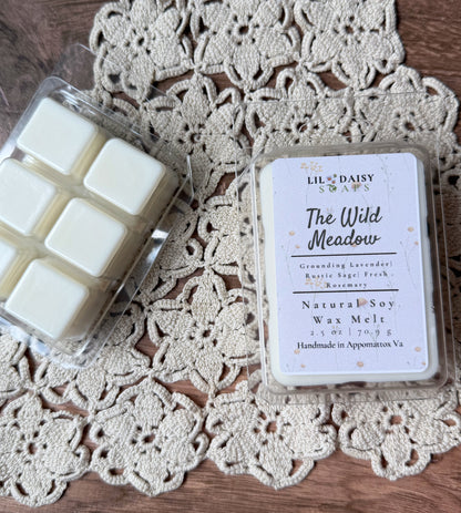 Two Lil Daisy Soaps wax melt packs rest on lace, one Wild Meadow with herbal lavender fragrance.